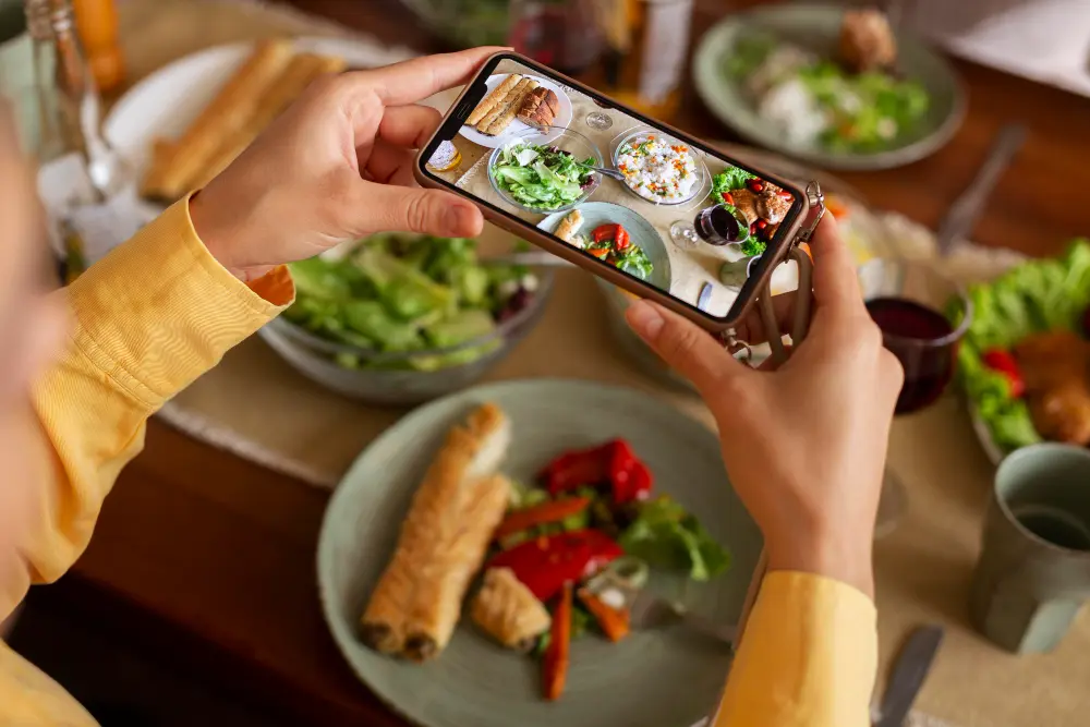 Close up das mãos de uma pessoa segurando um smartphone para tirar uma foto da refeição que está fazendo para o registro alimentar